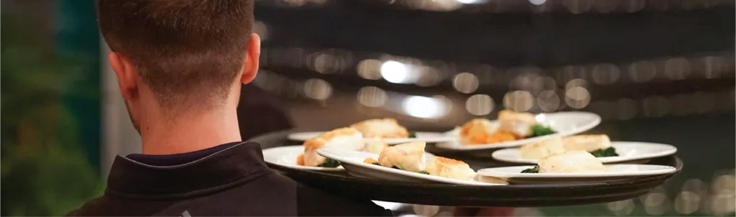 Catering server carrying multiple plated meals at an event