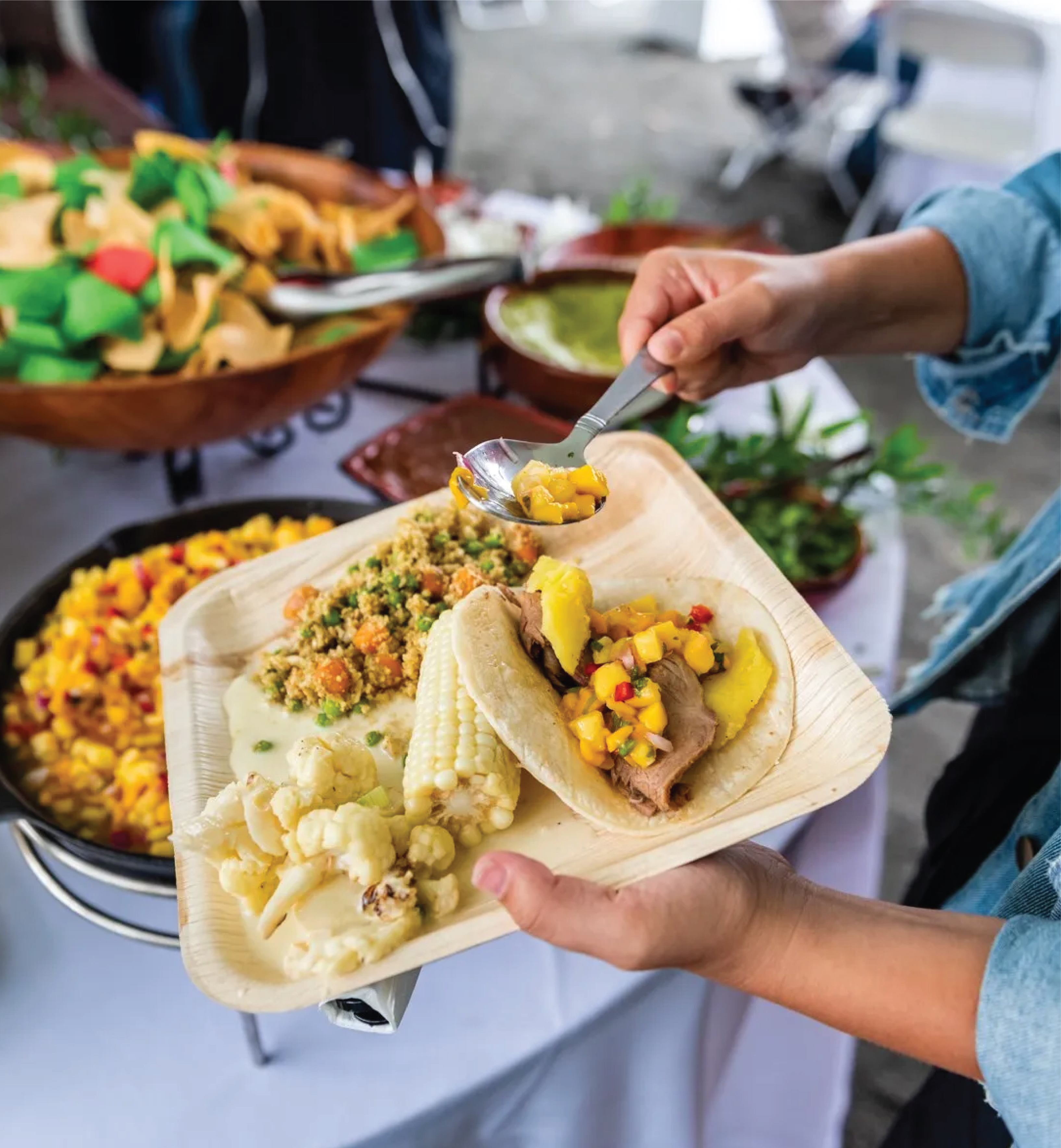 Guest serving taco with mango salsa and fresh sides at a catered buffet