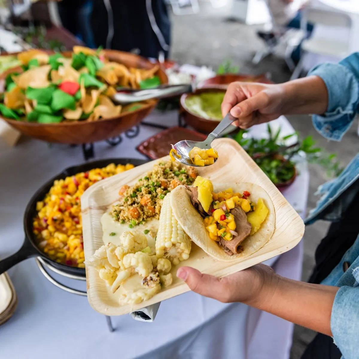 Guest adding mango salsa to taco with fresh sides at a catered buffet